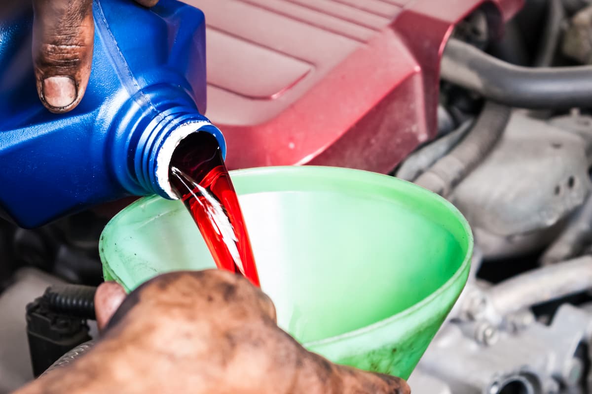 A man's hand pouring transmission fluid through a green funnel.