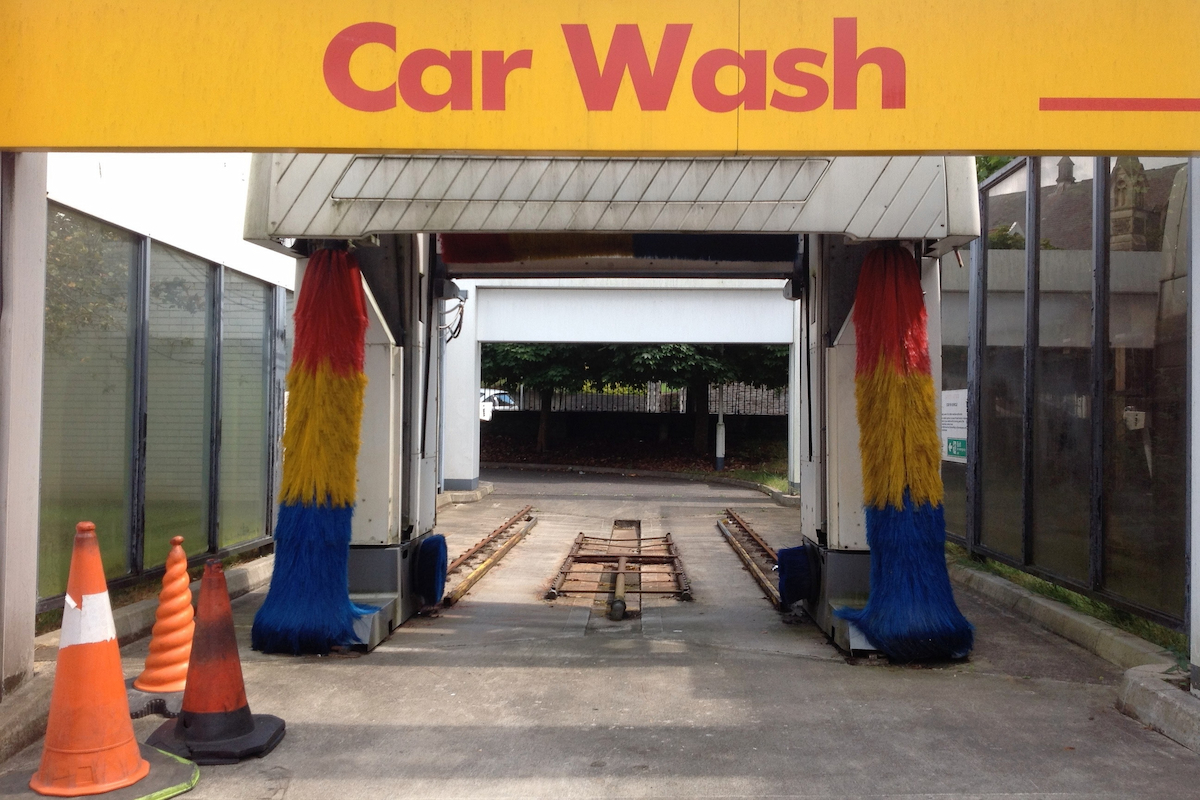 A view of a car washing machine with multicolored rolls and three traffic cones in front of it.