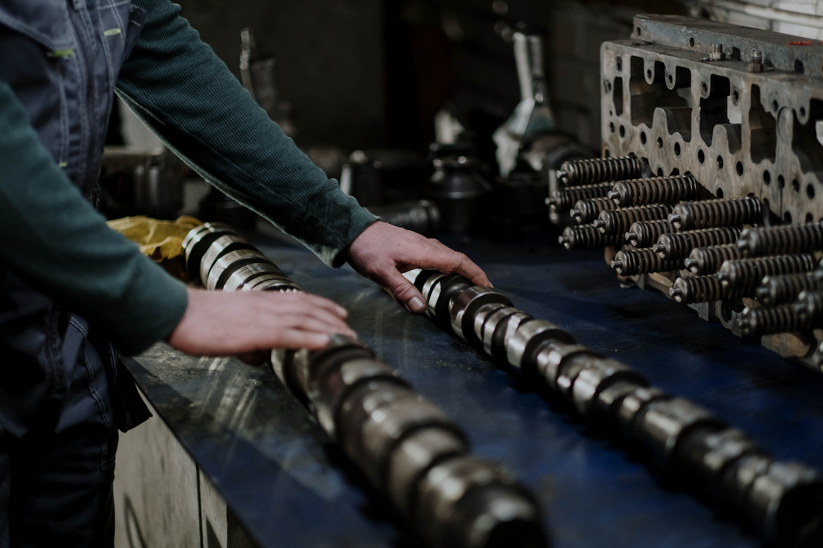 A man in long sleeve shirt holding a performance camshaft.
