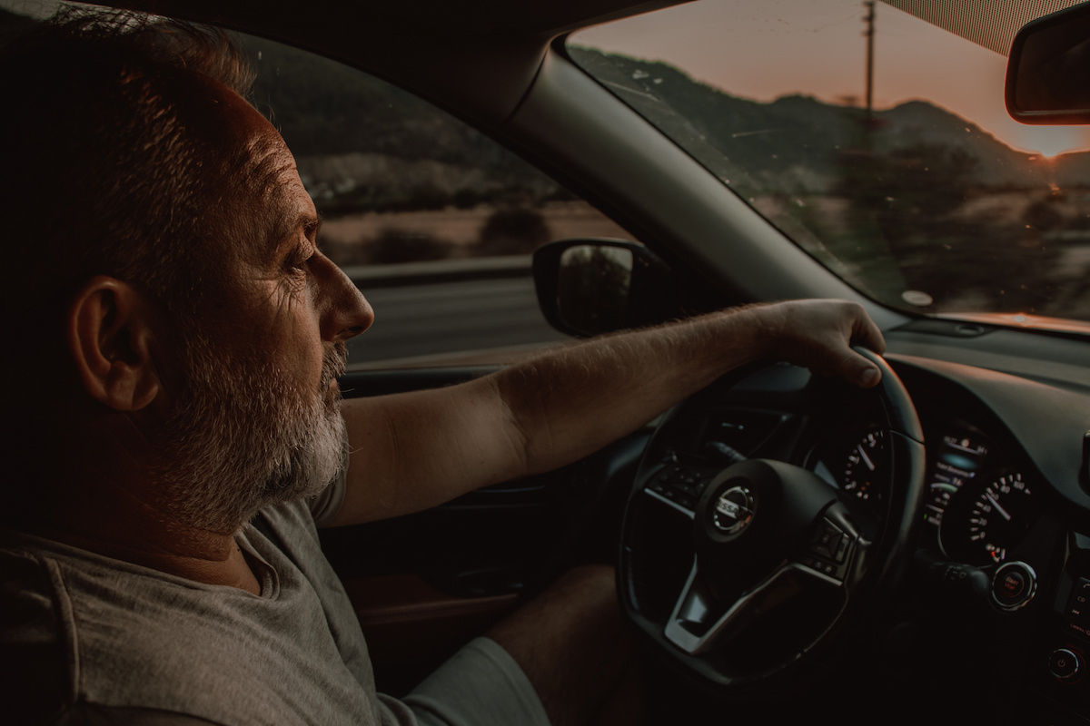 An old man using his left hand to drive a vehicle.