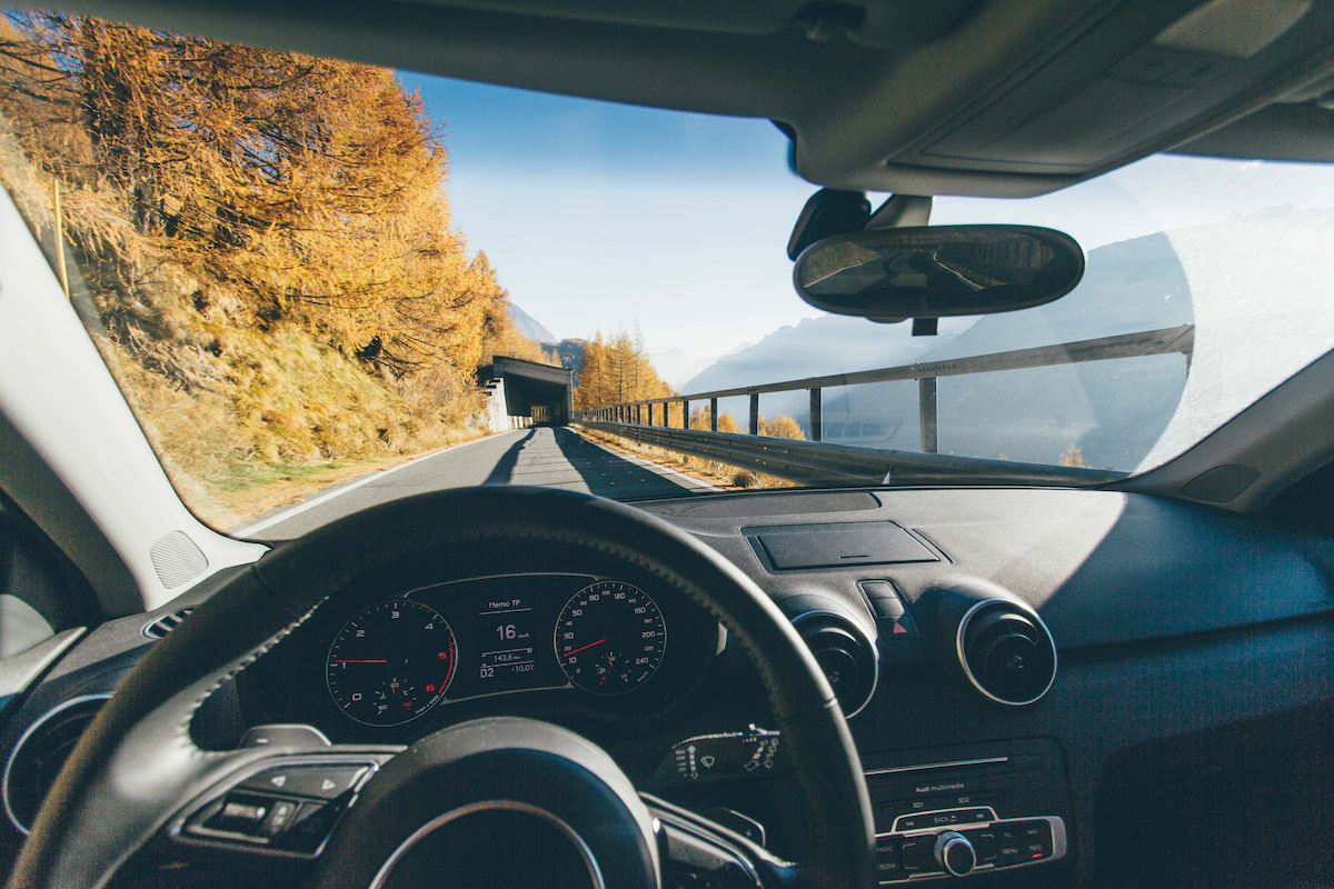 A car drives approaching a tunnel on a road lined by trees.