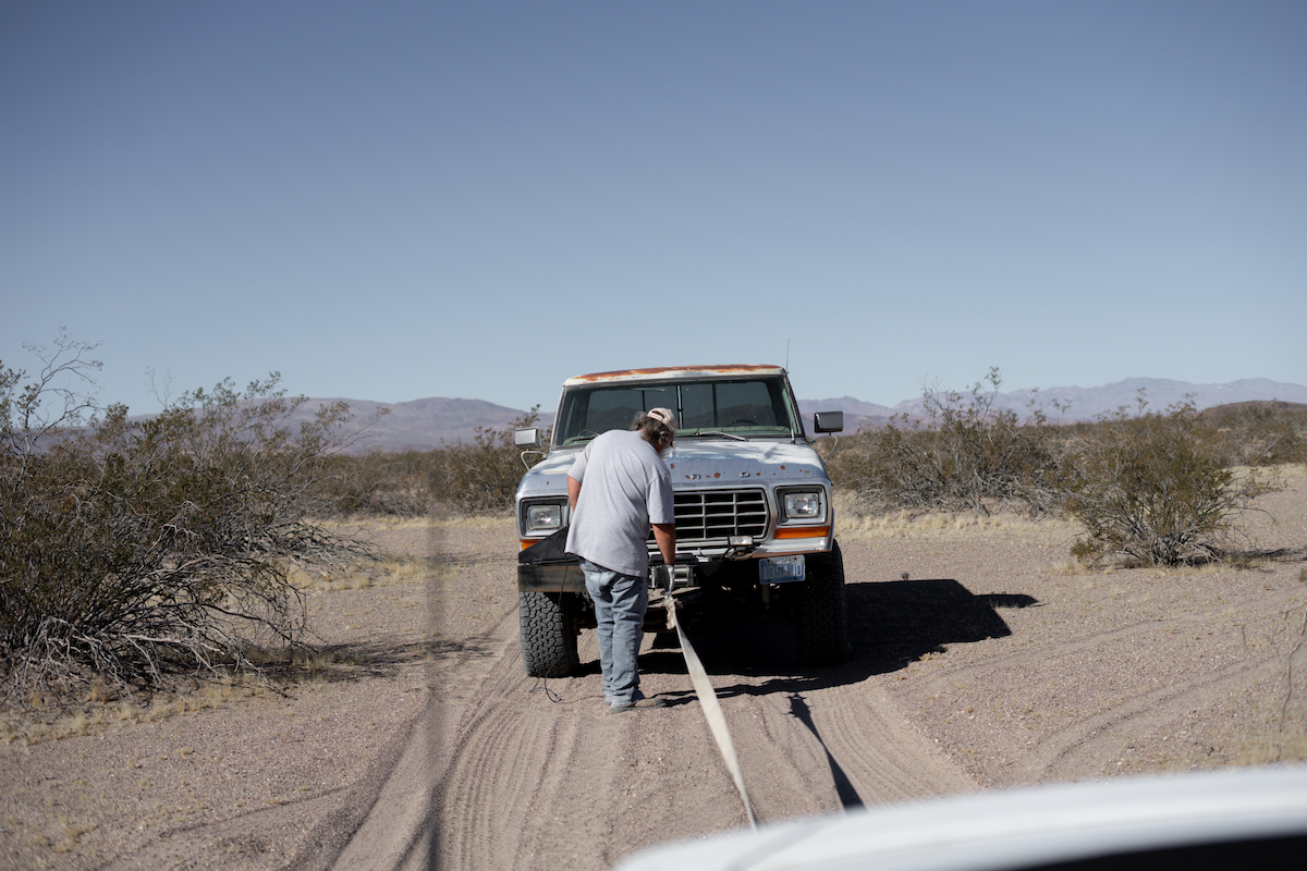 A man preparing to tow a pickup truck on a desert road.