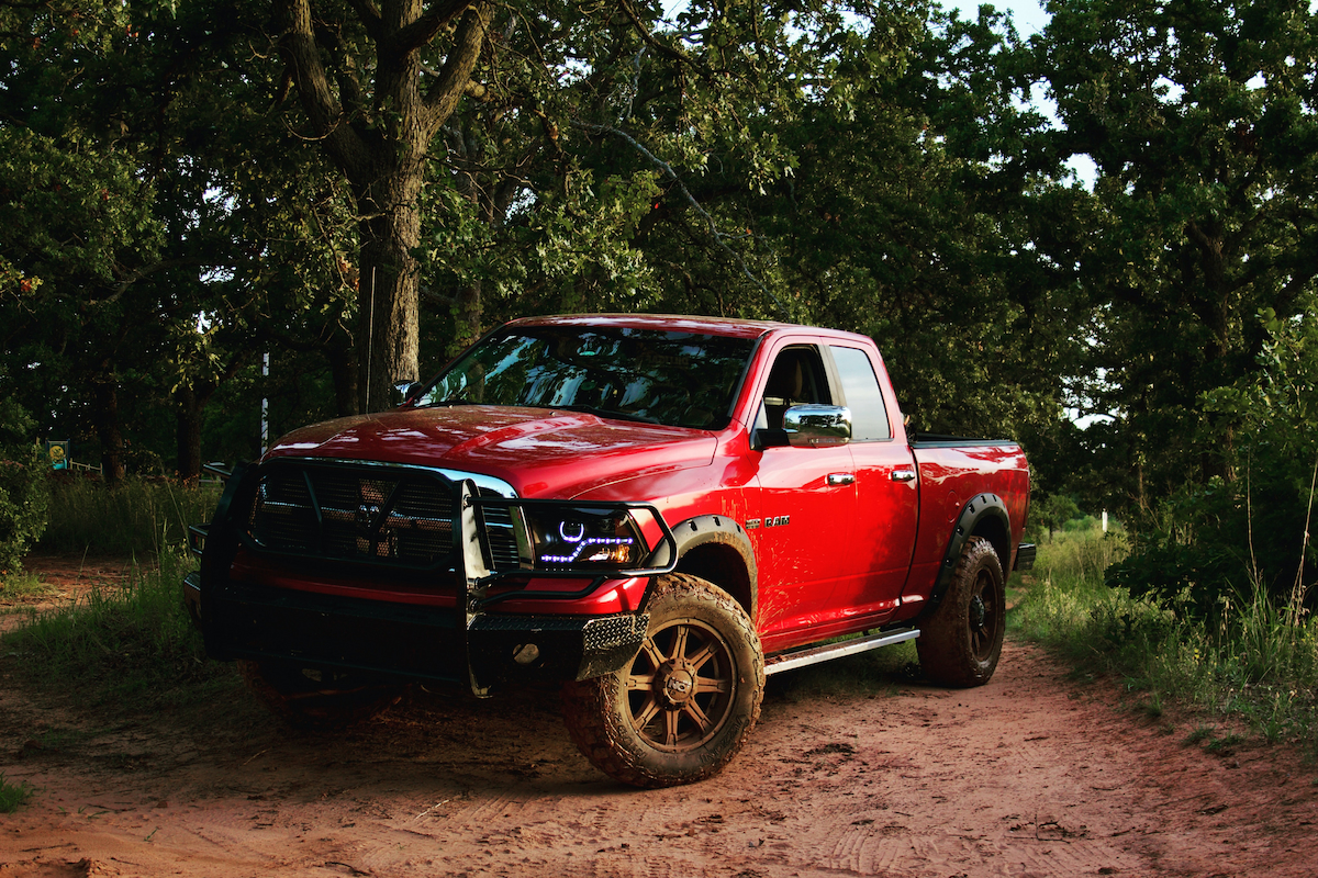 A red pickup up truck with muddy wheels in the woods.