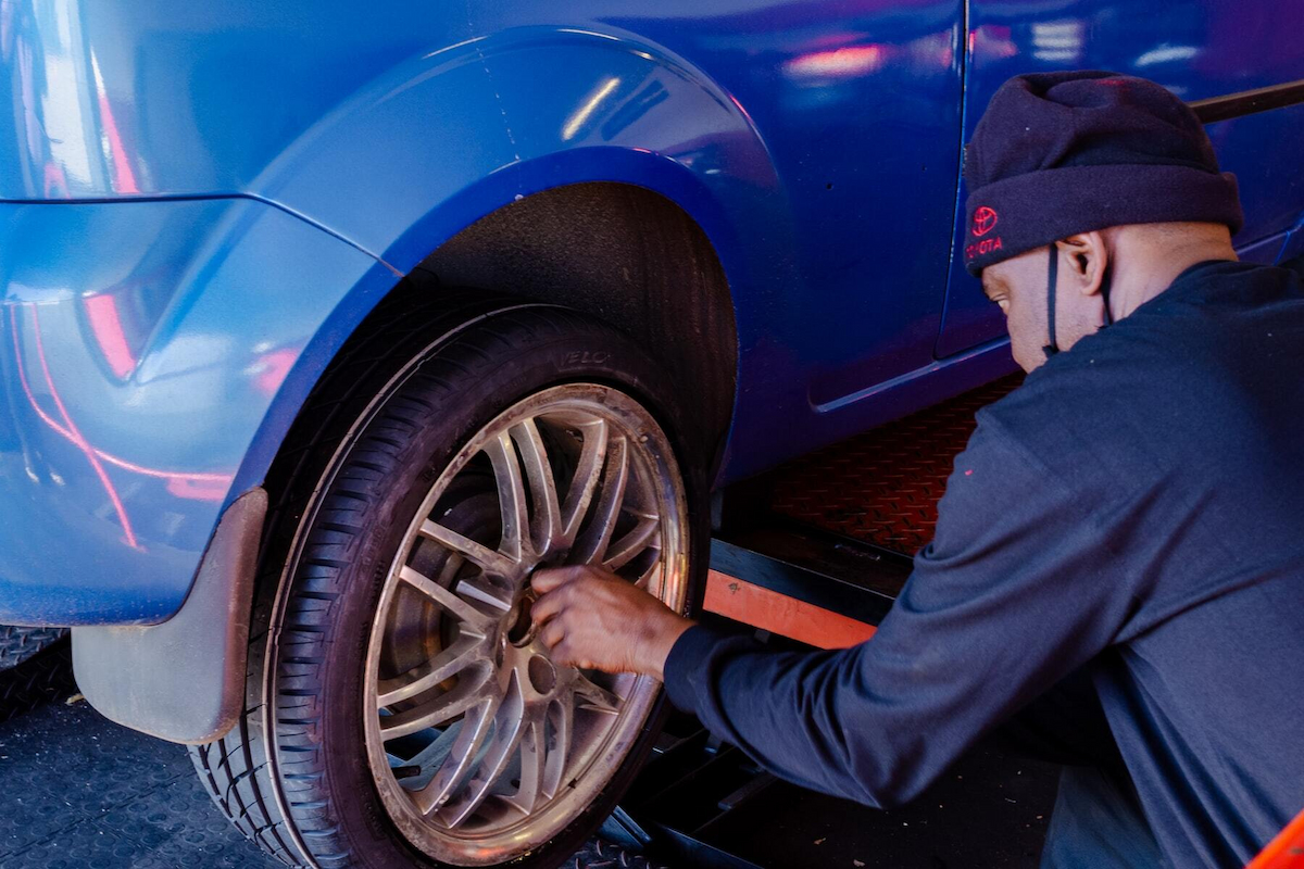 a man in dark blue suit is changing the tire of a blue car