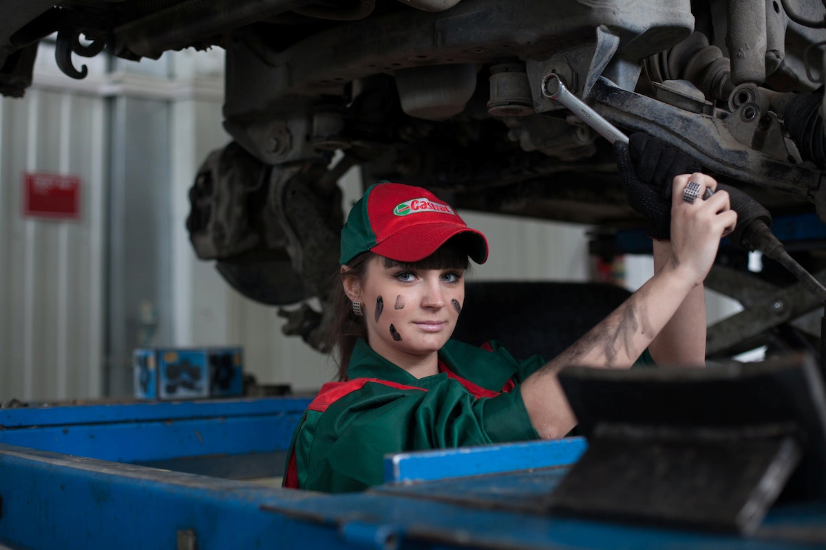 a woman wearing a green and red uniform and a cap is fixing a vehicle