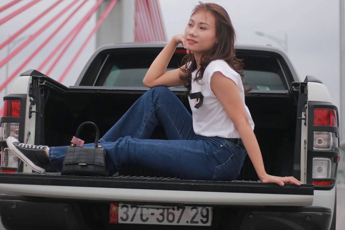 a young woman on a casual wear is sitting on a pick up truck's bed