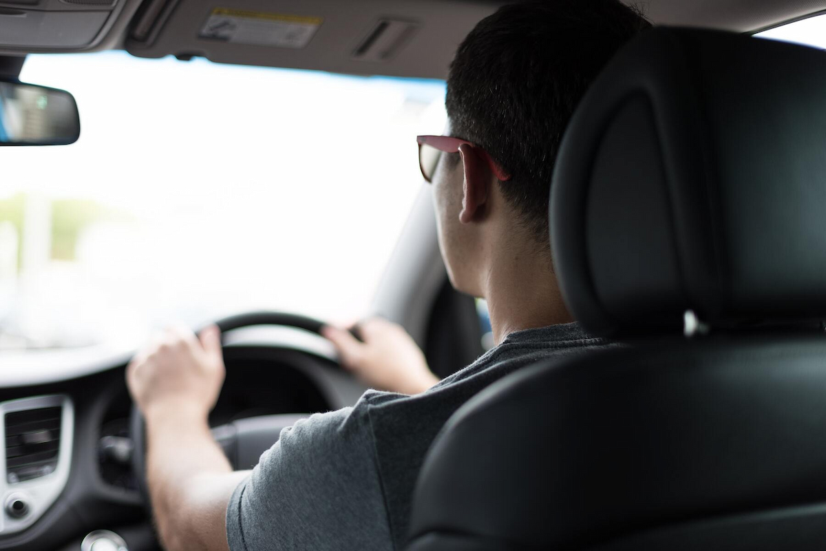 a man wearing eyeglasses and gray shirt is driving a car