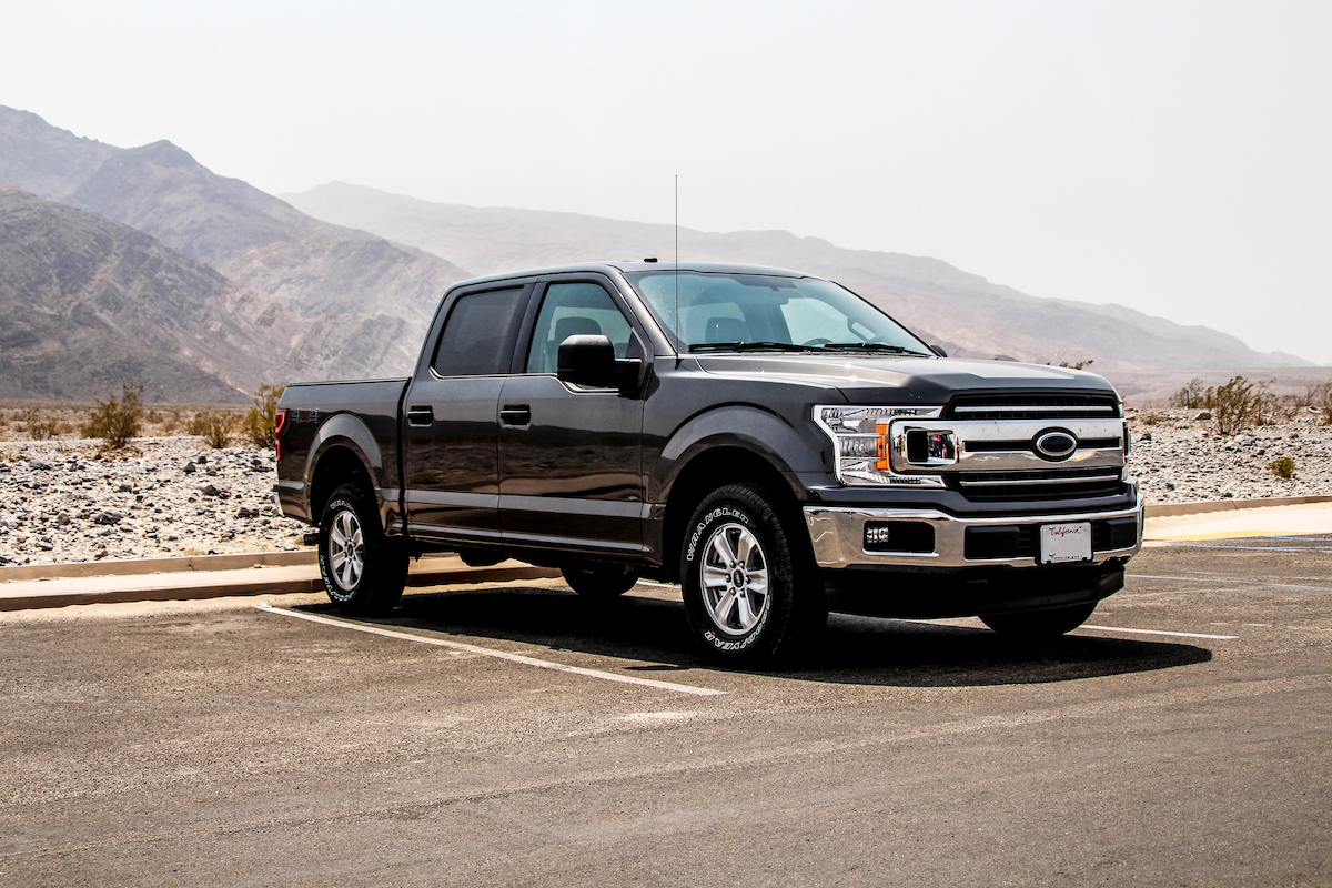 A black pickup truck parked on a road behind a mountain.