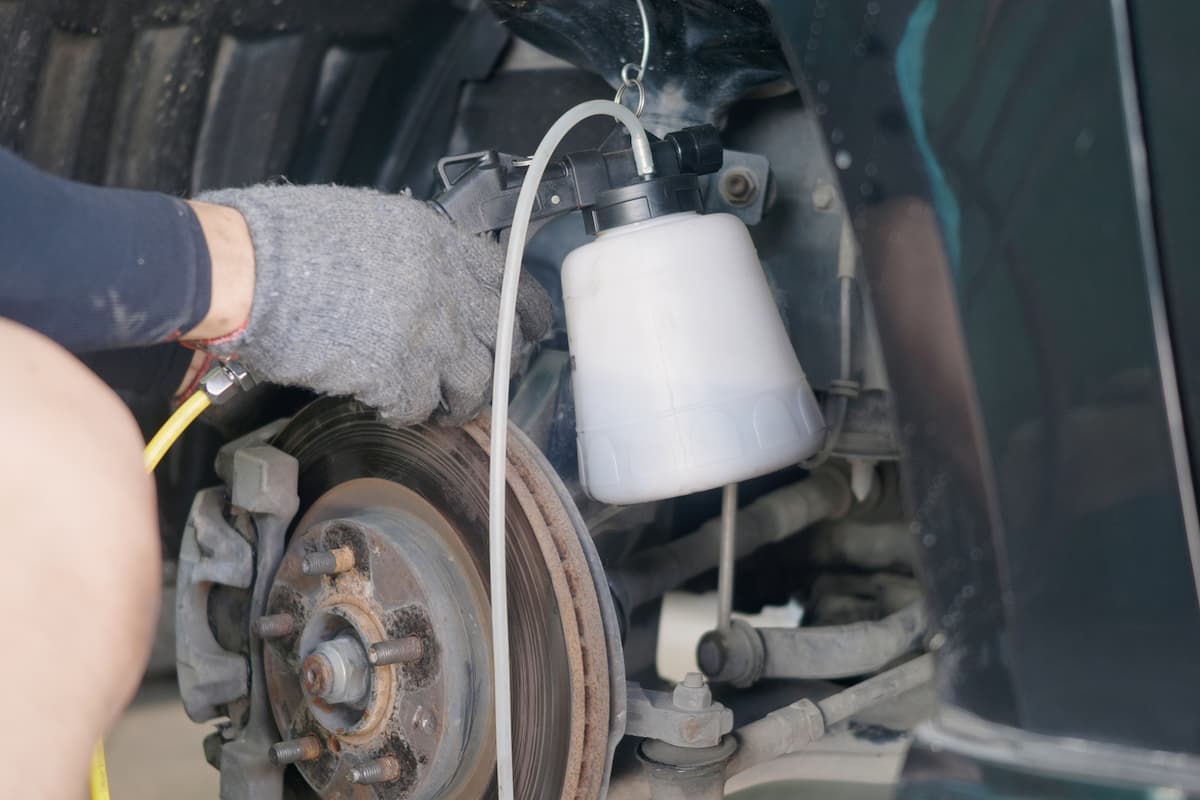 A mechanic wearing gray gloves bleeds air out of disc brake system in a car repair service. 