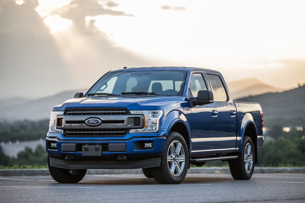 A blue Ford F-150 parked on a road during sunrise. 