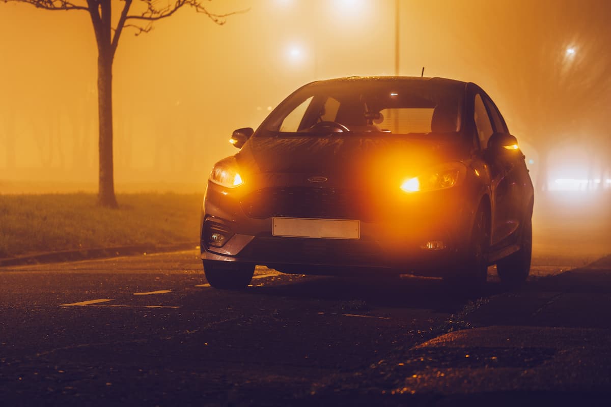 A car parked on a foggy road during sunset with its blinkers on. 