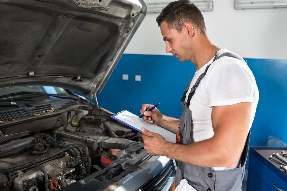 A mechanic holding a clipboard and checking the car for inspection at repair service. 
