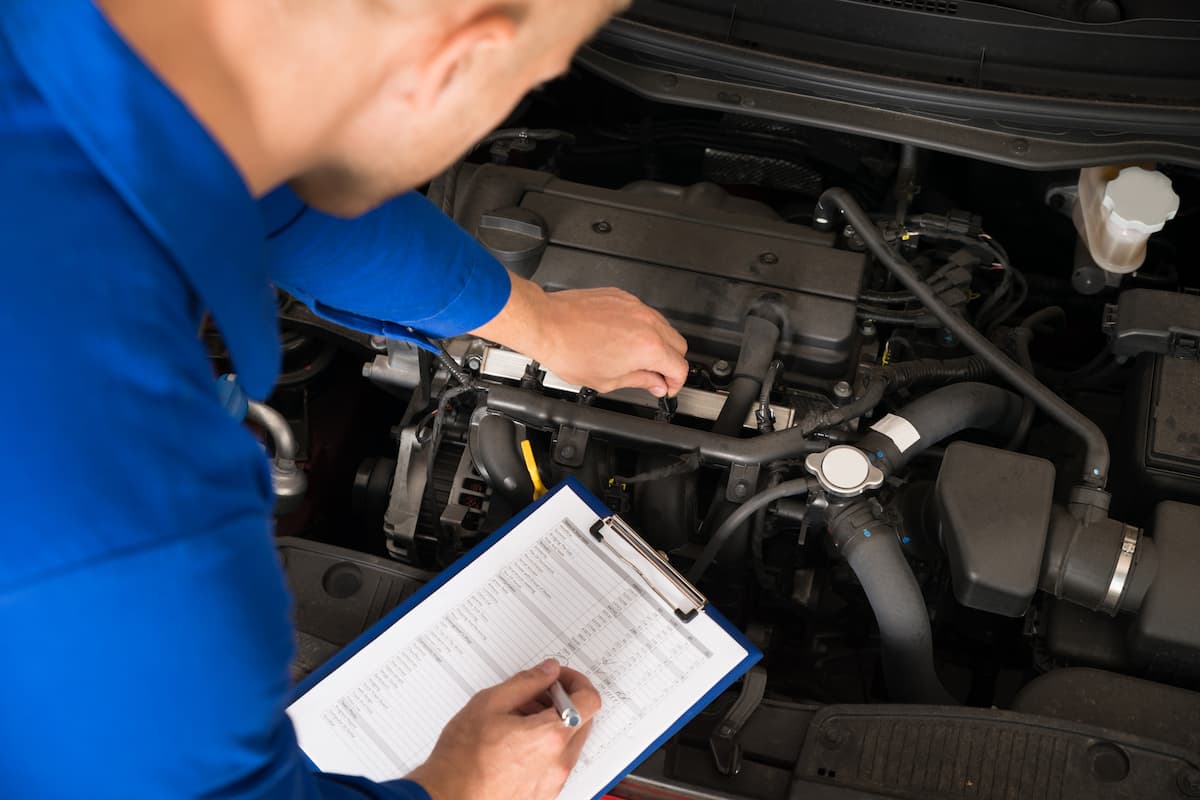 A mechanic standing near a car is writing on the clipboard in a car garage. 