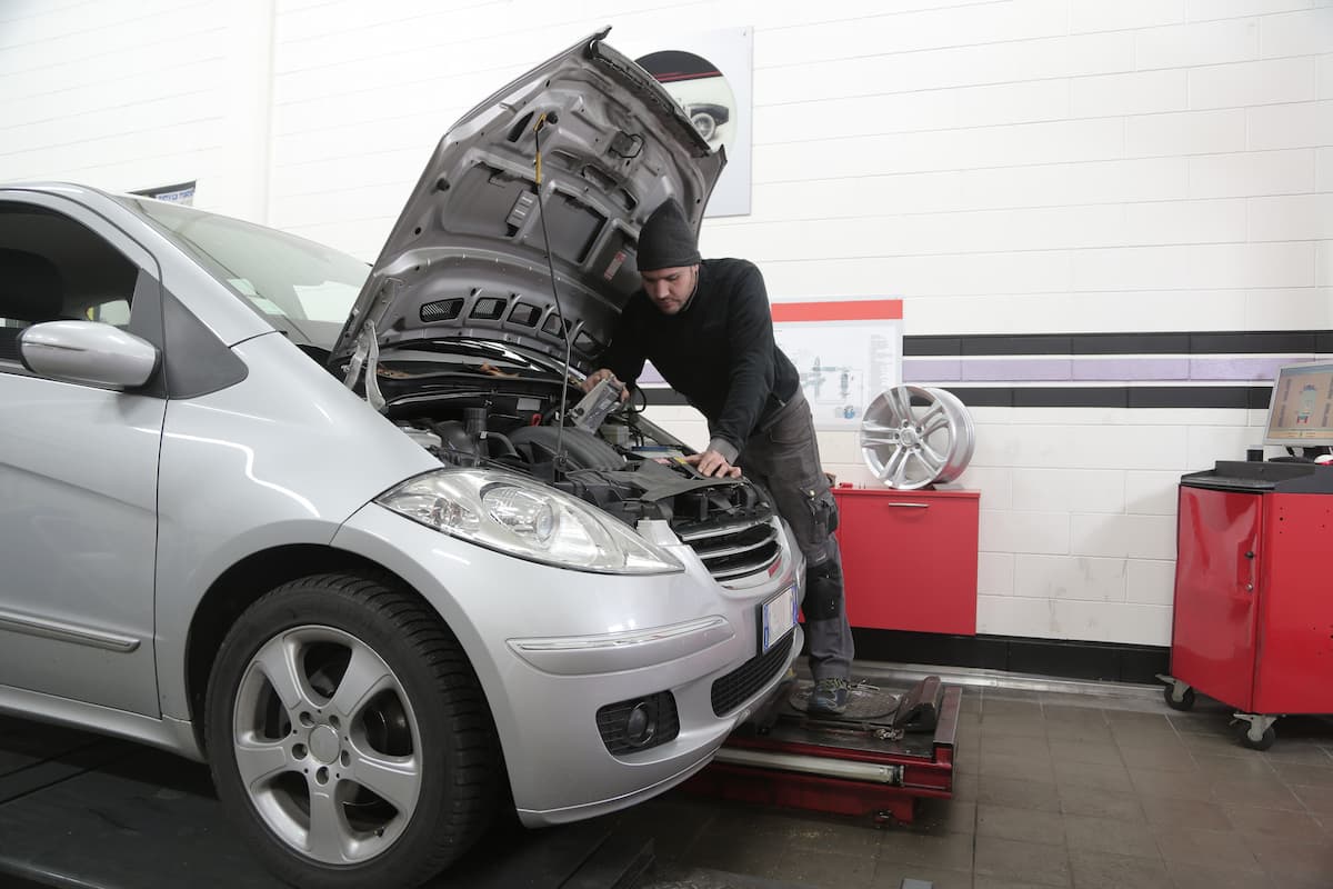 A mechanic wearing a black sweater and a black hood is checking the car's engine. 