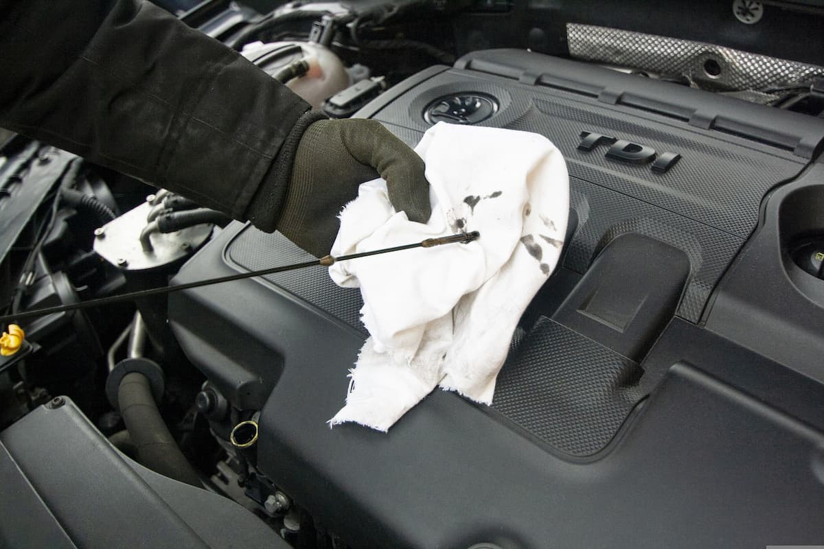 A mechanic wearing gloves changing an engine oil.