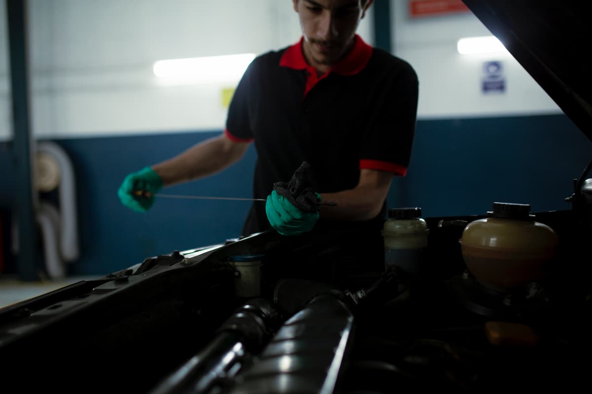 A man with green gloves is checking the engine oil of a car.