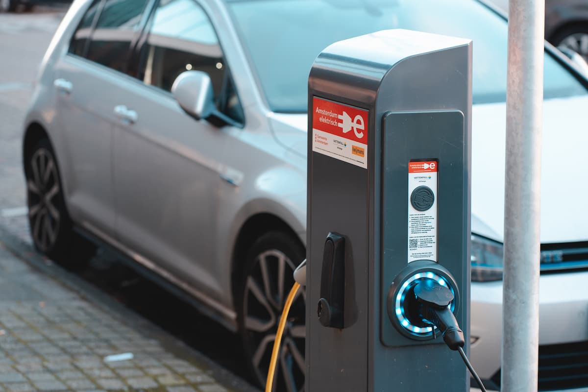 A photo of an electric car charger charging a white electric car. 