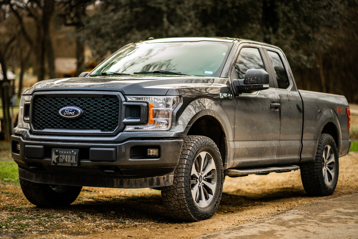 A dusty, black Ford F-150 parked on a dirt road.