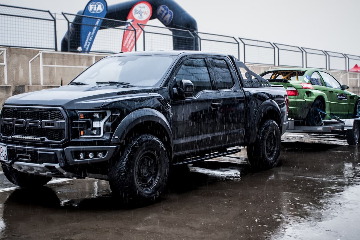 A black Ford pickup truck flat towing a green car in the rain.