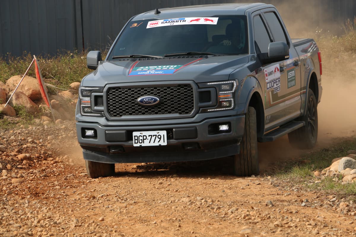 A gray Ford pickup truck driving on a dusty and rock road. 