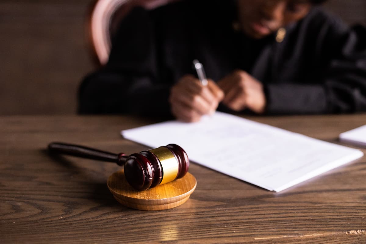 A wooden gavel on a wooden table and a blurred judge signing on a paper. 