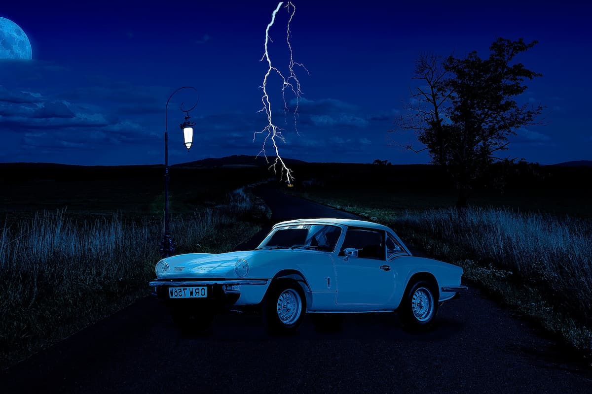 A car on a field and lightning strikes in the middle of the road. 