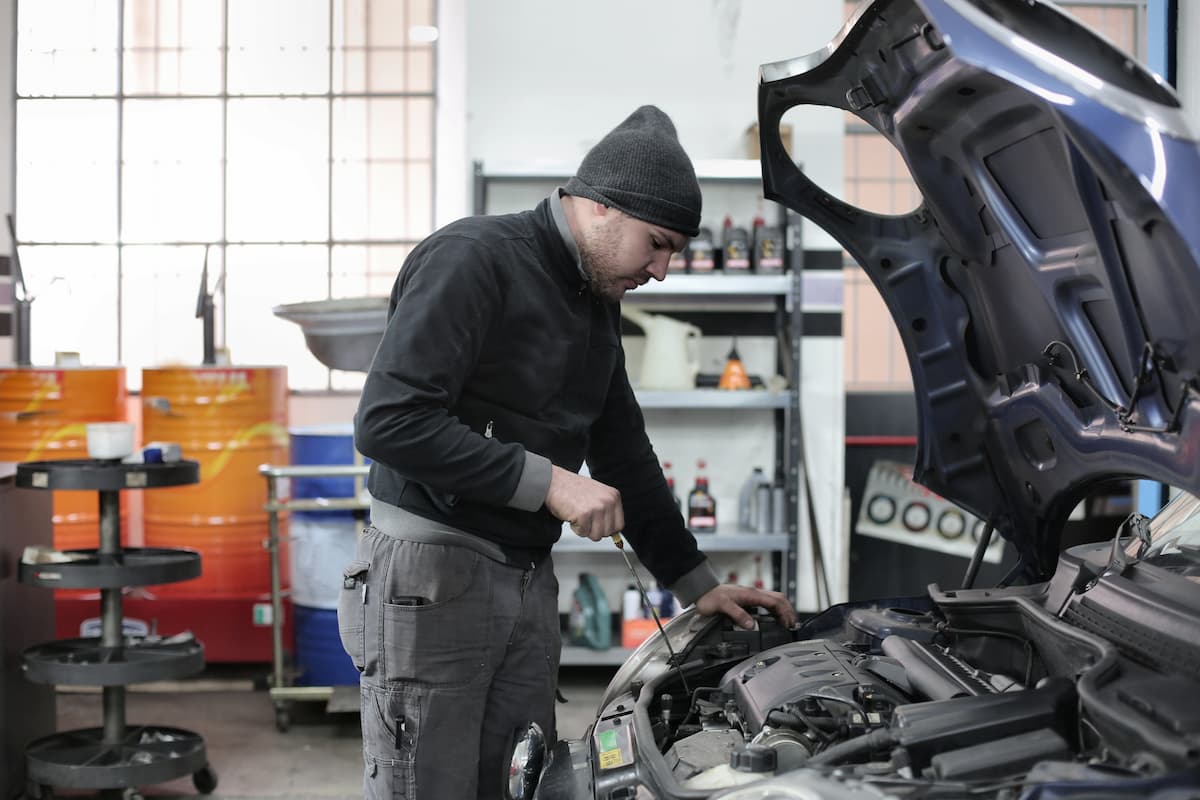 A man wearing a black sweater and a black hood checking the car's engine.