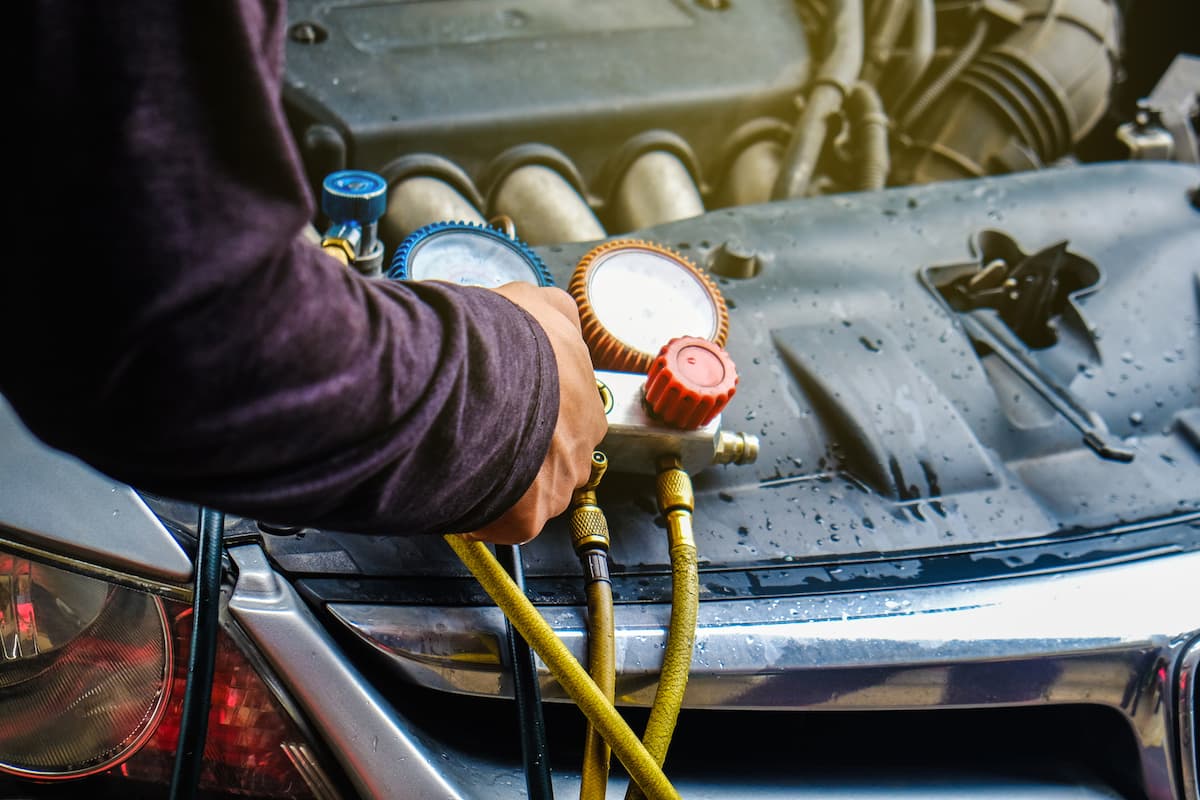 A photo of a man's hand wearing a maroon sweater is adding freon to a car.