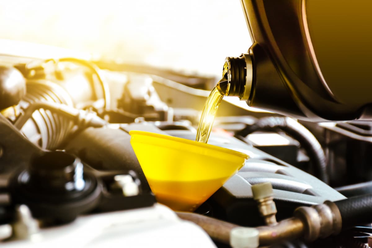 A mechanic pouring motor oil into engine through a yellow funnel. 