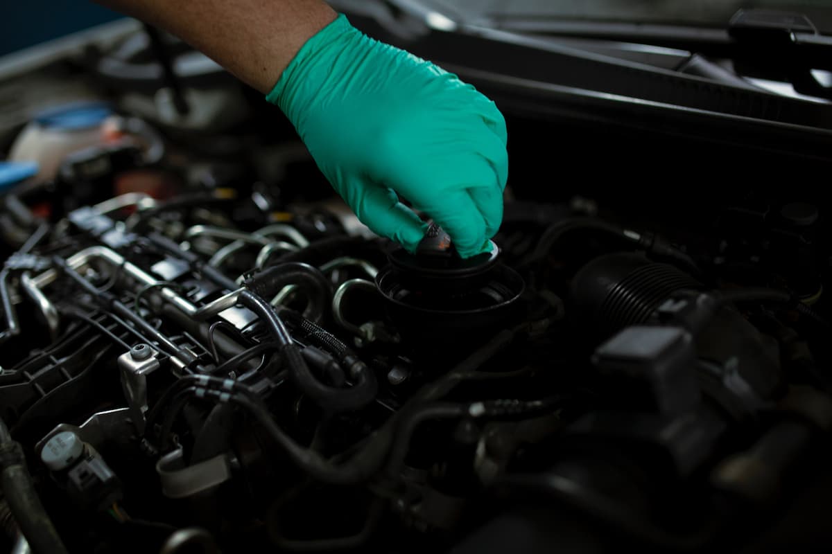 A mechanic opening the oil filler cap of a car engine. 
