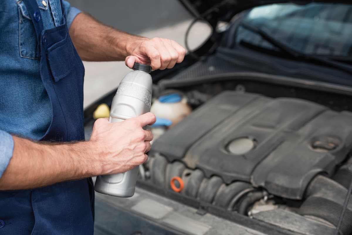 A mechanic in uniform opening a bottle of motor oil near a blurred car. 