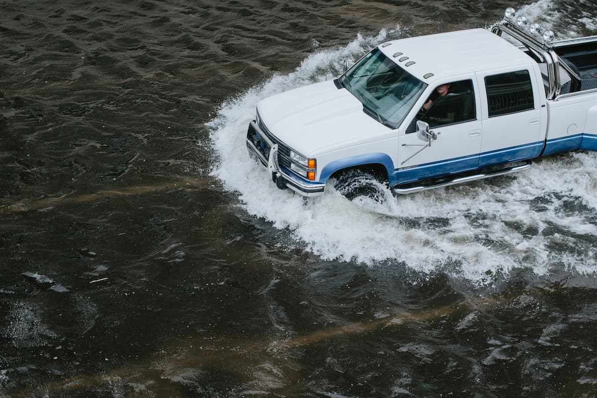 A white pickup truck driving through the flood. 