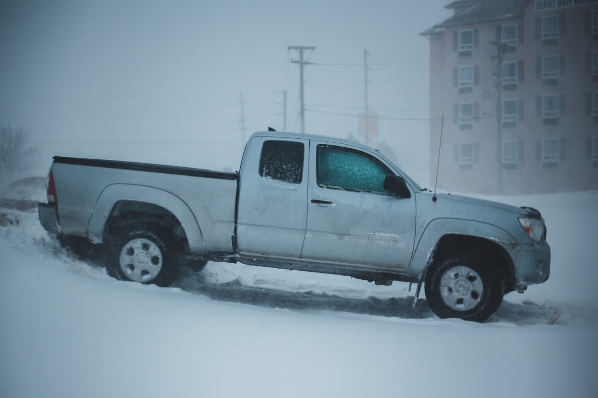 A white pickup truck parked on a snowy road on a snowy day. 