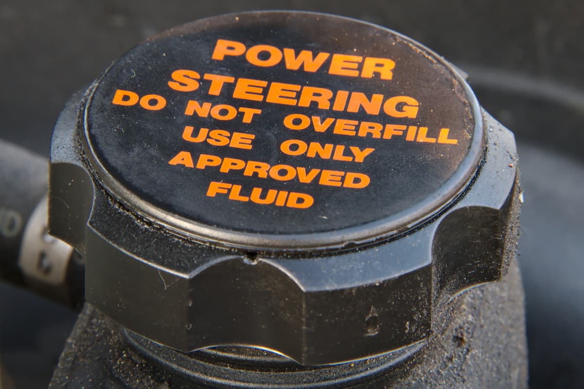 Close-up of a cap of a power steering oil tank with a warning text, "Do not overfill and use approved fluid only."