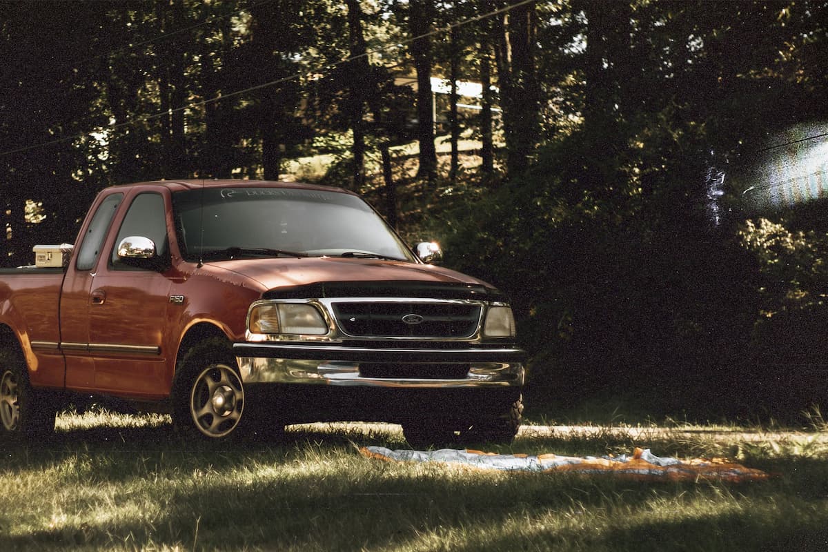 A red Ford pickup truck parked in the grass near trees. 