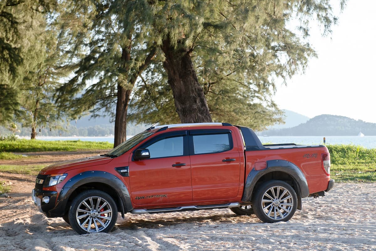 A red Ford pickup truck parked at beach near the trees. 