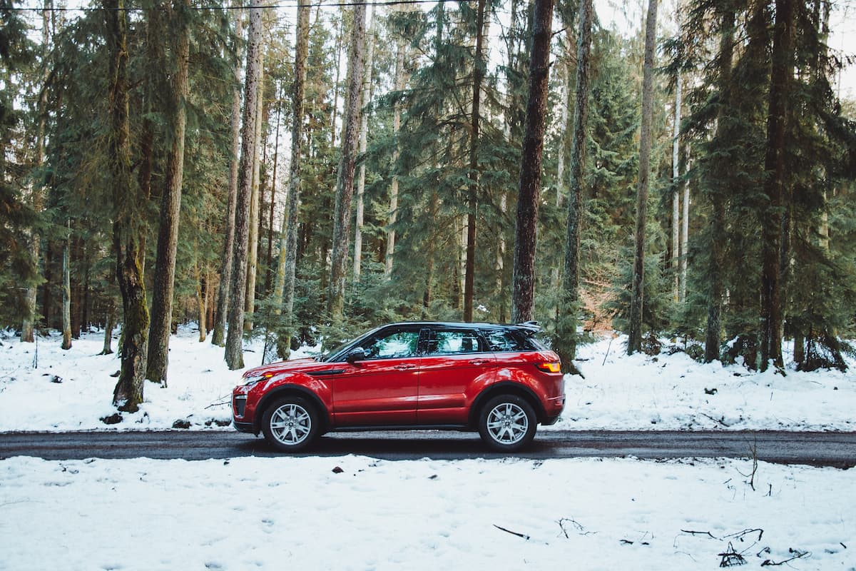 A red SUV parked on a snowy road near tall trees. 