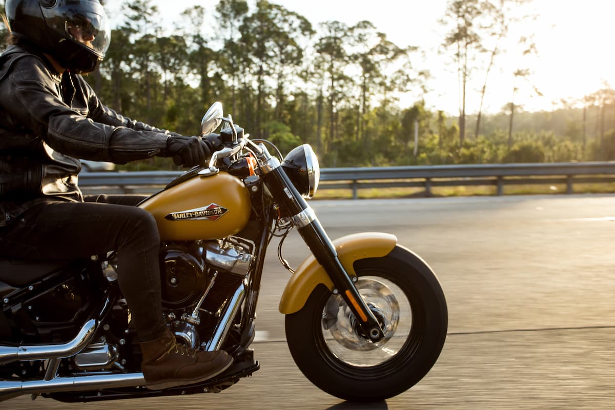 A man wearing a black jacket, black helmet, and brown boots is riding a yellow motorcycle. 