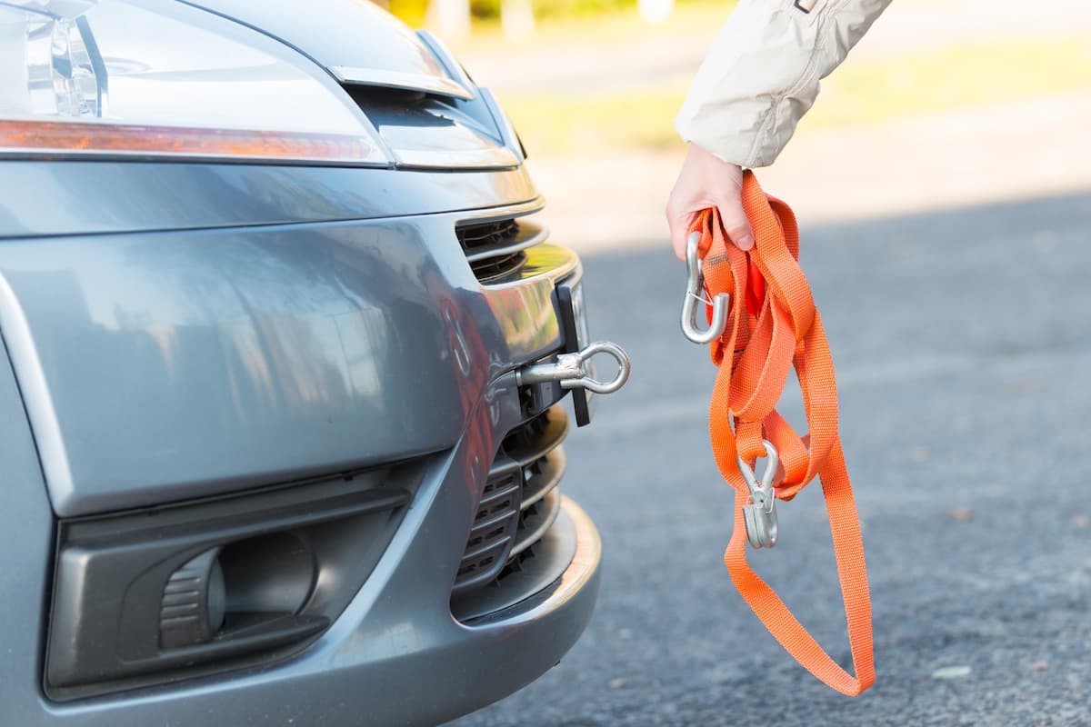 A woman's hand holding tow rope near a towing hook attached to a car.