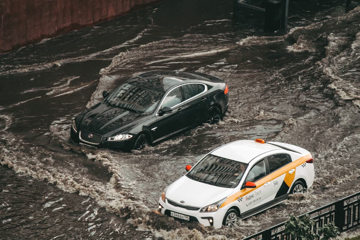 A black car and a taxi driving through the flood. 