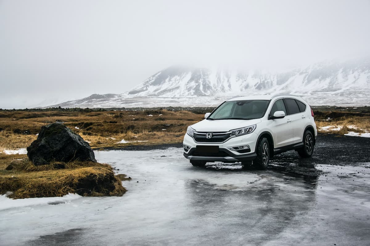A white Honda CR-V on a frozen lake with a mountain covered in snow in the background.