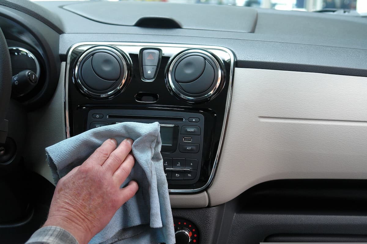 Photo of an old man's hand wiping a car's dashboard with a microfiber cloth.